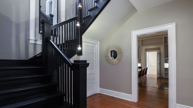 Eine Treppe mit schwarzen Geländern und einer Lampe. Eine weiße Tür und ein Spiegel sind an der Wand angebracht.