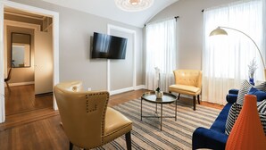 Ein modernes Wohnzimmer mit einem Flachbildfernseher, Ledersesseln, einem blauen Sofa und einem gemusterten Teppich.