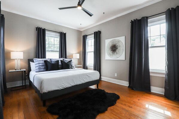 A bedroom with a bed, a ceiling fan, a black rug, and a window with curtains.