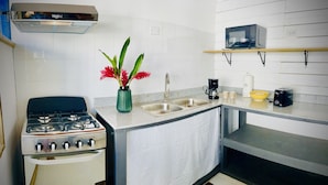 A kitchen with a gas stove, double sink, microwave, and a shelf with a coffee maker and cups. - Apartamentos Casa Le Parc (Bocas del Toro)