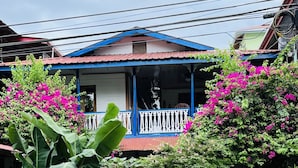 A house with a blue balcony, surrounded by lush greenery and pink flowers. - Apartamentos Casa Le Parc (Bocas del Toro)
