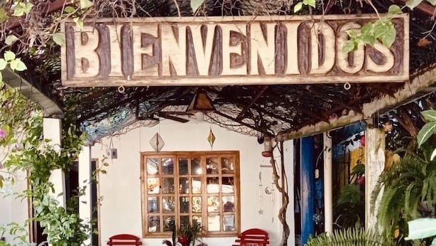 A wooden sign reading "BIENVENIDOS" above a pathway leading to a building with a tiled floor and potted plants. - Apartamentos Casa Le Parc (Bocas del Toro)