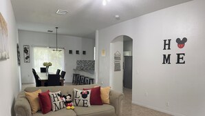 Un salon avec un canapé beige, une table basse blanche et un tapis rouge. Un mur est décoré des mots « HOME » et du logo de Mickey Mouse.