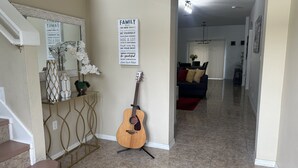 Un salon avec une guitare, un panneau décoratif sur le thème de la famille et un escalier menant à une autre pièce.