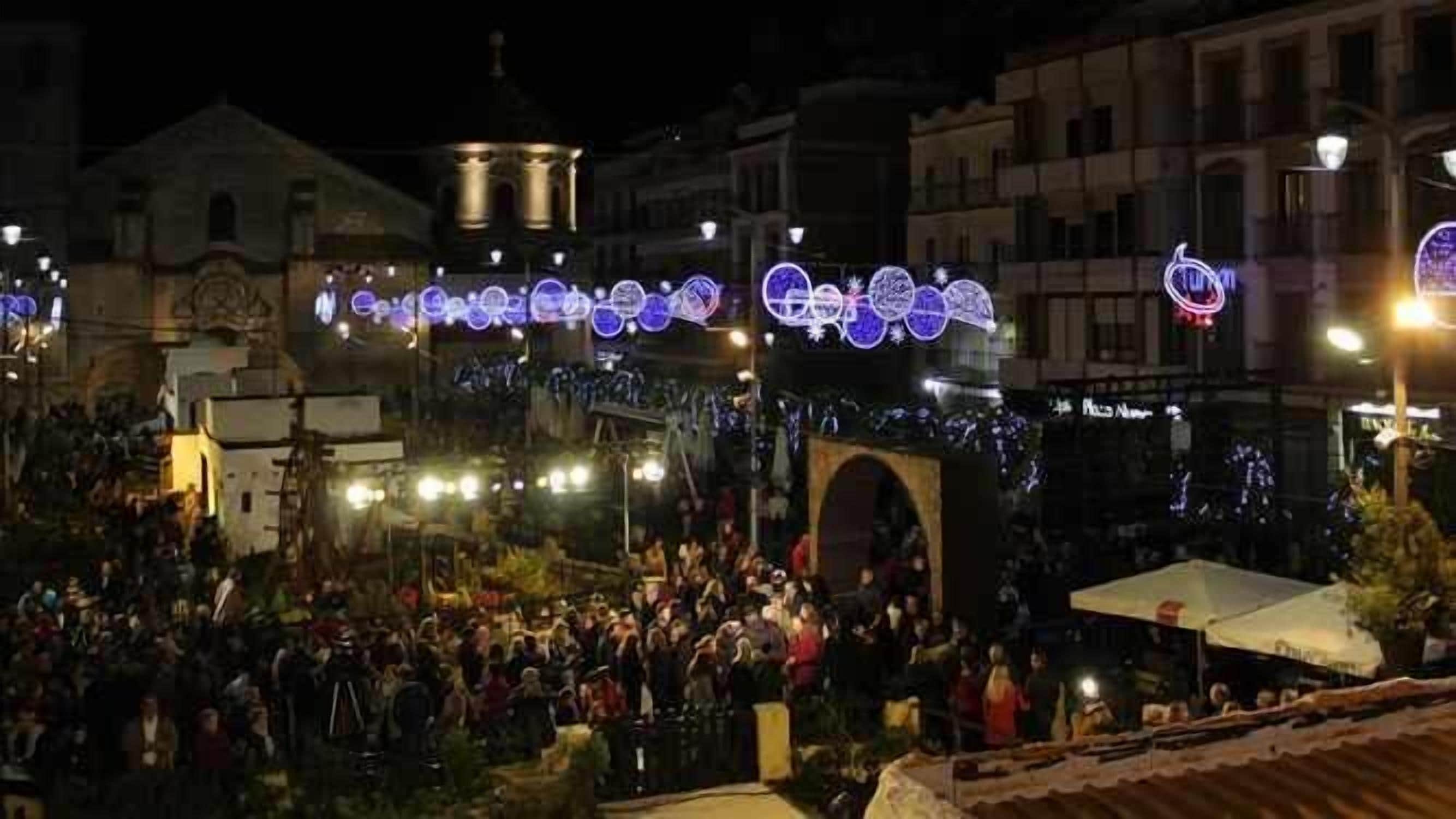Una plaza concurrida con arcos iluminados y gente.