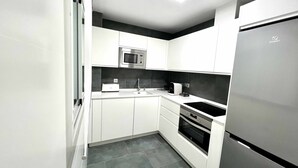 Una cocina moderna con armarios blancos, microondas integrado, tostadora y refrigerador de acero inoxidable.