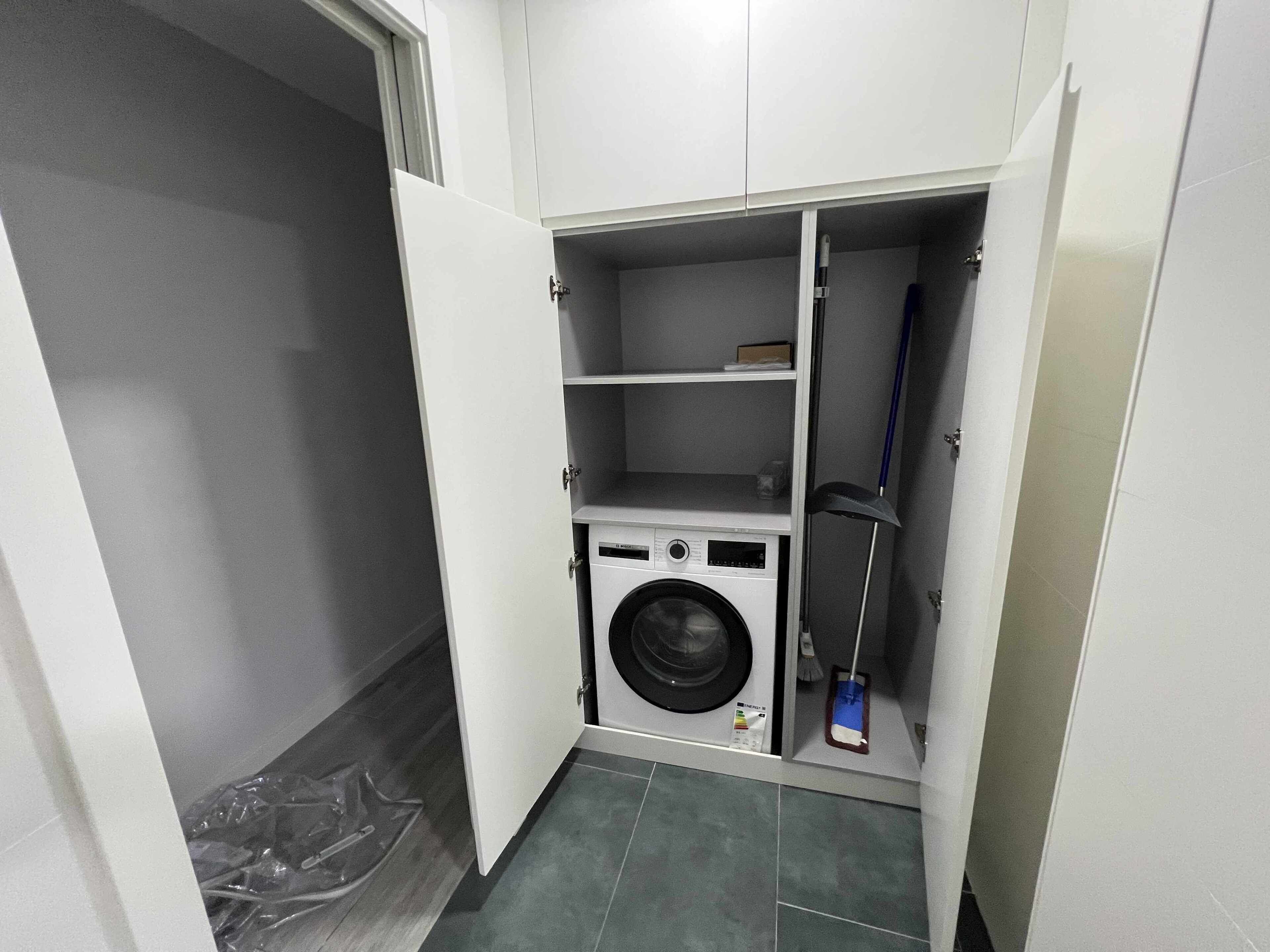 A compact laundry room with a washing machine, shelves, and a mop.
