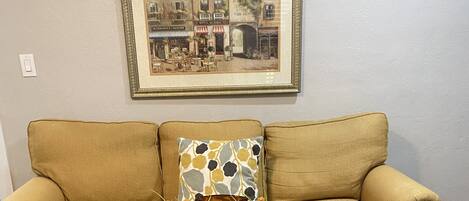 A living room with a glass-top coffee table, a sofa, and a framed picture on the wall.