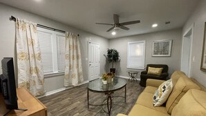 A living room with a sofa, a coffee table, a TV stand, and a ceiling fan. - Charming City Bungalow (Jacksonville)