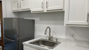 A kitchen with white cabinets, a stainless steel refrigerator, a sink with a faucet, and marble countertops. - Charming City Bungalow (Jacksonville)