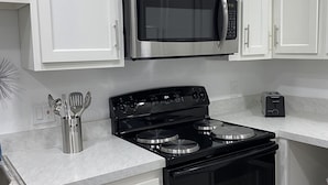 A modern kitchen with white cabinets, a stainless steel microwave, a black stove, and a toaster. - Charming City Bungalow (Jacksonville)