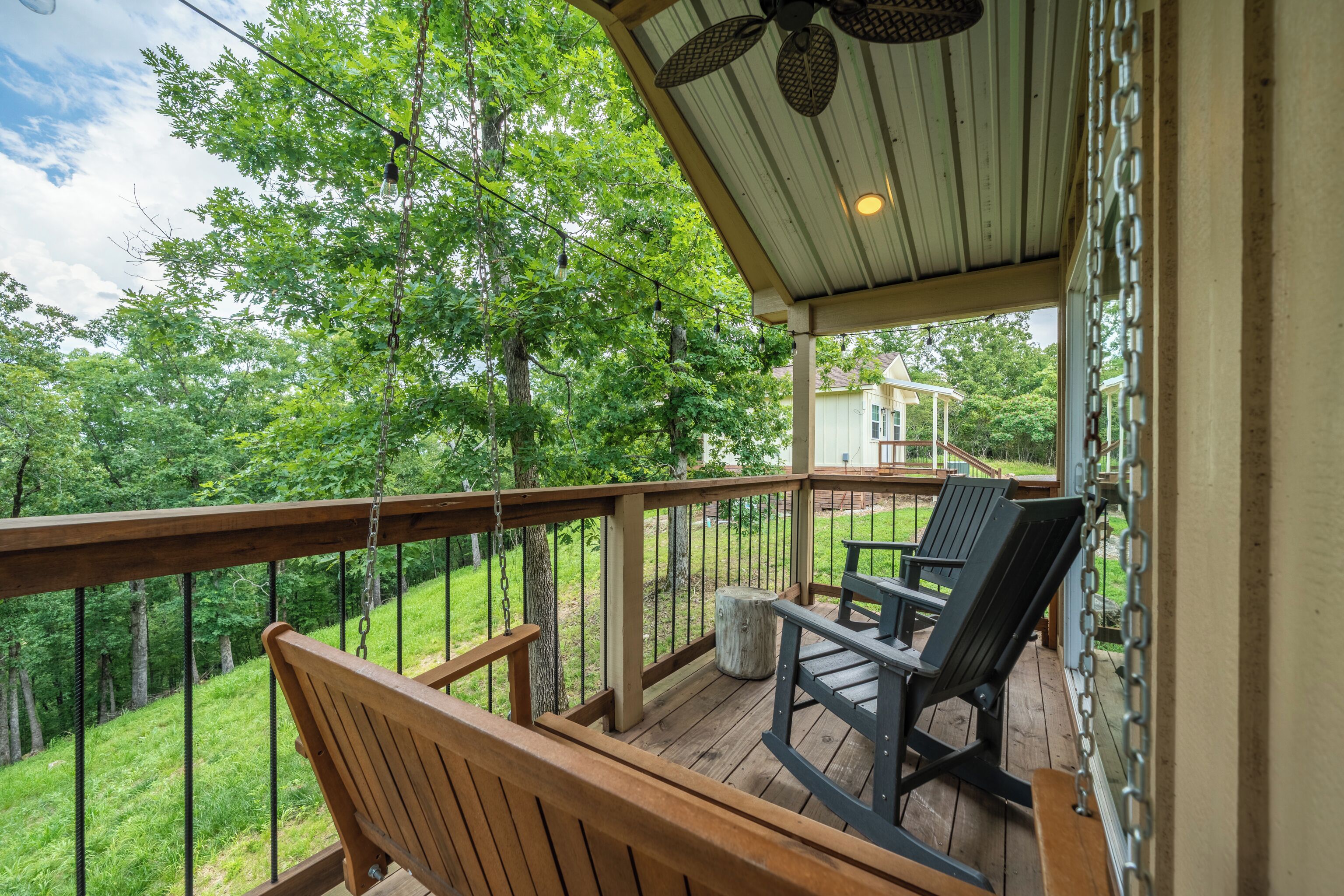 A wooden deck with a bench and two chairs, overlooking a grassy area and trees.