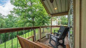 A wooden deck with a bench and two chairs, overlooking a grassy area and trees.