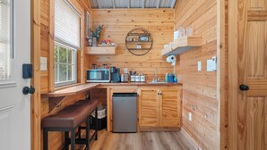 Una cocina compacta con paredes de madera, microondas integrado, lavamanos y un refrigerador pequeño.