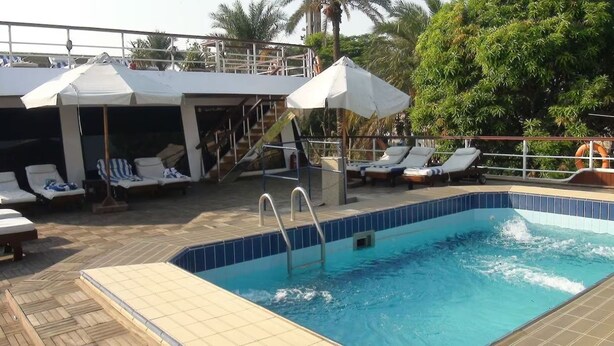 A swimming pool with lounge chairs and umbrellas, a staircase leading to an upper deck, and palm trees in the background. - River Boat - Double Room with Private Bathroom (Cairo)