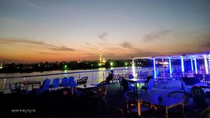 An outdoor seating area with tables and chairs, overlooking a body of water with a distant tower. - River Boat - Double Room with Private Bathroom (Cairo)
