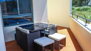 A balcony with a glass-top table and wicker chairs, a window with a metal grill, and a view of greenery. - Breakers 1/3- Stone Real Estate Yamba (Yamba)