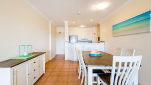 Una cocina moderna con armarios blancos, una mesa de comedor de madera y un cuadro en la pared.