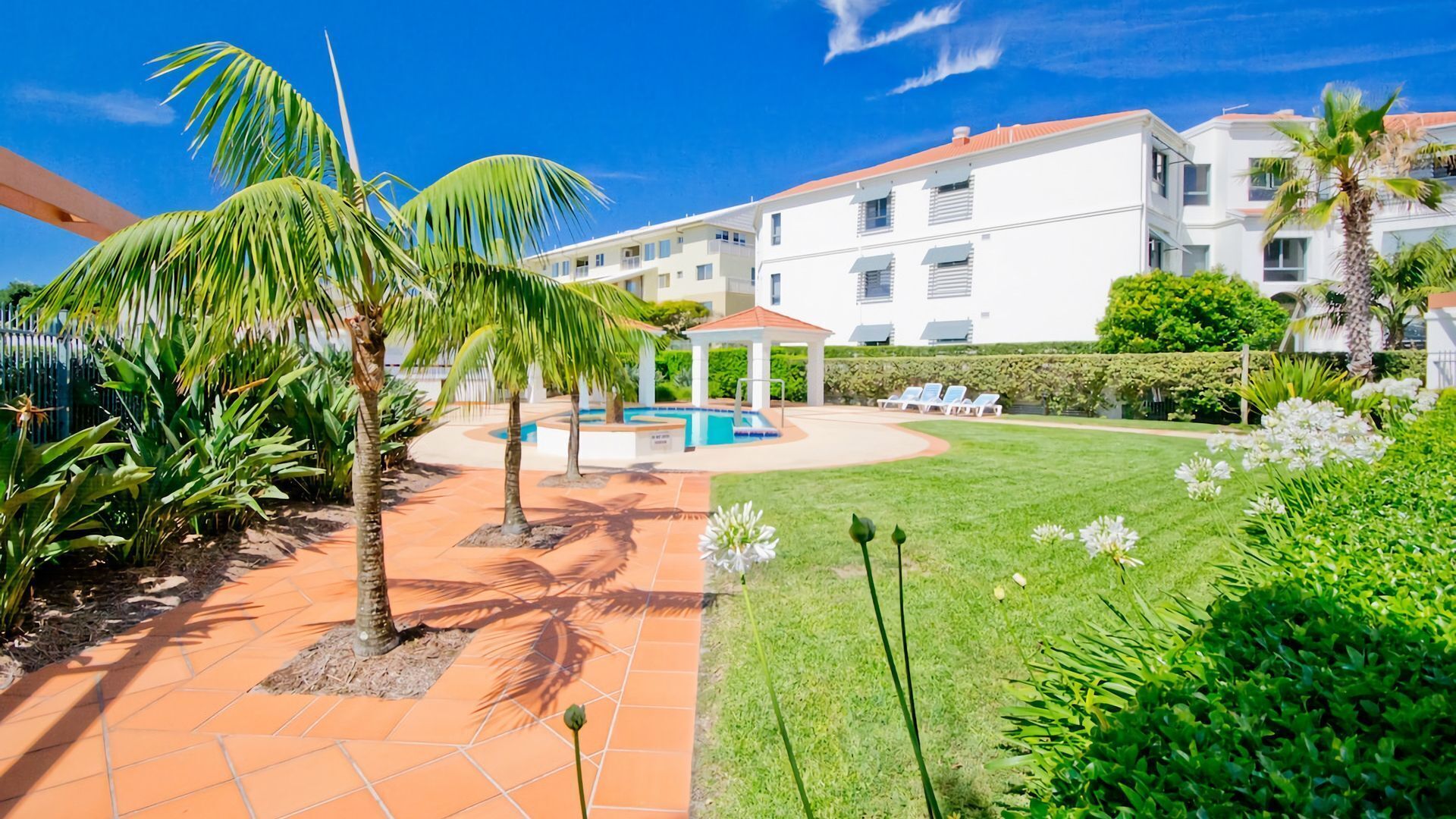 Une cour avec une piscine, des palmiers et un bâtiment blanc doté de balcons.