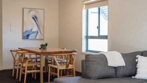 A room with a dining table and chairs, a gray sofa, and a window with blinds. - Breakers 1/8- Stone Real Estate Yamba (Yamba)