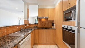 A modern kitchen with wooden cabinets, a stainless steel sink, a built-in oven, and a microwave. - Breakers 1/8- Stone Real Estate Yamba (Yamba)