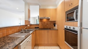 Una cocina moderna con armarios de madera, un lavamanos de acero inoxidable, un horno empotrado y un microondas.