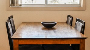 A rectangular dining table with a dark bowl in the center, surrounded by six chairs with dark upholstery. - Seaspray 8 - Stone Real Estate Yamba (Yamba)