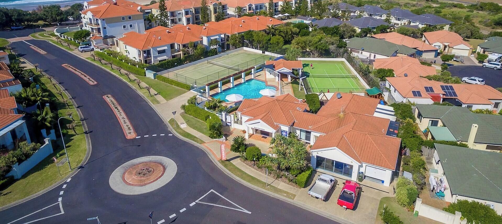 A residential area with a roundabout, houses with red roofs, a swimming pool, and tennis courts.