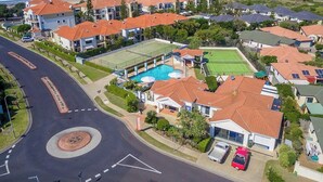 A residential area with a roundabout, houses with red roofs, a swimming pool, and tennis courts. - Seaspray 8 - Stone Real Estate Yamba (Yamba)