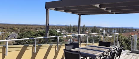 A balcony with a wooden table and chairs, overlooking a residential area with houses and trees.