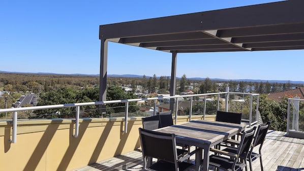 A balcony with a wooden table and chairs, overlooking a residential area with houses and trees.
