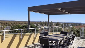 Un balcón con mesa y sillas de madera, con vista a una zona residencial con casas y árboles.
