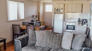 A compact living space with a kitchenette, a dining area, and a seating area with a sofa. - Seaspray 8 - Stone Real Estate Yamba (Yamba)