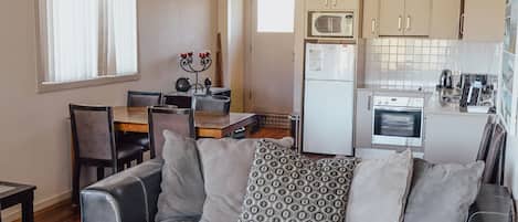 Un espacio habitable compacto con kitchenette, comedor y zona de estar con sofá.