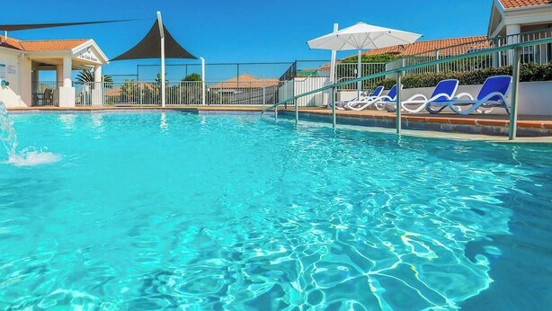 A swimming pool with clear blue water, surrounded by lounge chairs and umbrellas. - Seaspray 8 - Stone Real Estate Yamba (Yamba)