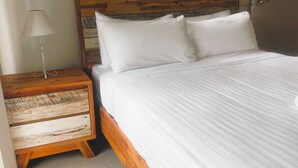 A bed with white bedding, a wooden nightstand with a lamp, and a headboard with a wooden panel design. - Seaspray 8 - Stone Real Estate Yamba (Yamba)