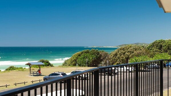 A coastal view with a beach, ocean, and parked cars.