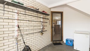 Una habitación con pared de ladrillo, cañas de pescar, un refrigerador pequeño y un enfriador azul.