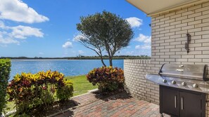 An outdoor patio with a grill, a view of a lake, and a tree.