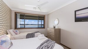 A bedroom with a bed, a dresser, a window with a view, and a ceiling fan.