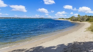 A beach with clear blue water, sandy shore, and trees in the background.