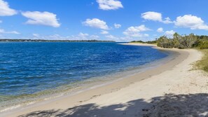 A beach with clear blue water, sandy shore, and trees in the background. - Peninsula Court 6- Stone Real Estate Yamba (Yamba)