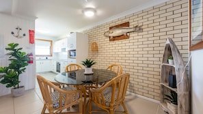 A modern kitchen with white cabinets, a brick accent wall, and a dining area with a glass table and wicker chairs.