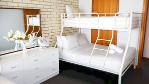 A bunk bed with a wooden headboard, a white dresser with drawers, a mirror, and a small fan on the dresser.