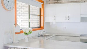 A kitchen with white cabinets, a window with an orange frame, a sink, and a clock on the wall.