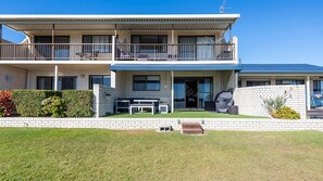 A two-story residential building with a balcony, a small outdoor seating area, and a well-maintained lawn.