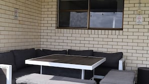 A corner seating area with a table and cushions, a brick wall, and a window.