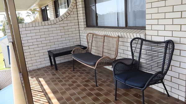 Un espace extérieur abrité, aménagé avec deux fauteuils en osier et un banc, un mur en briques et une fenêtre.