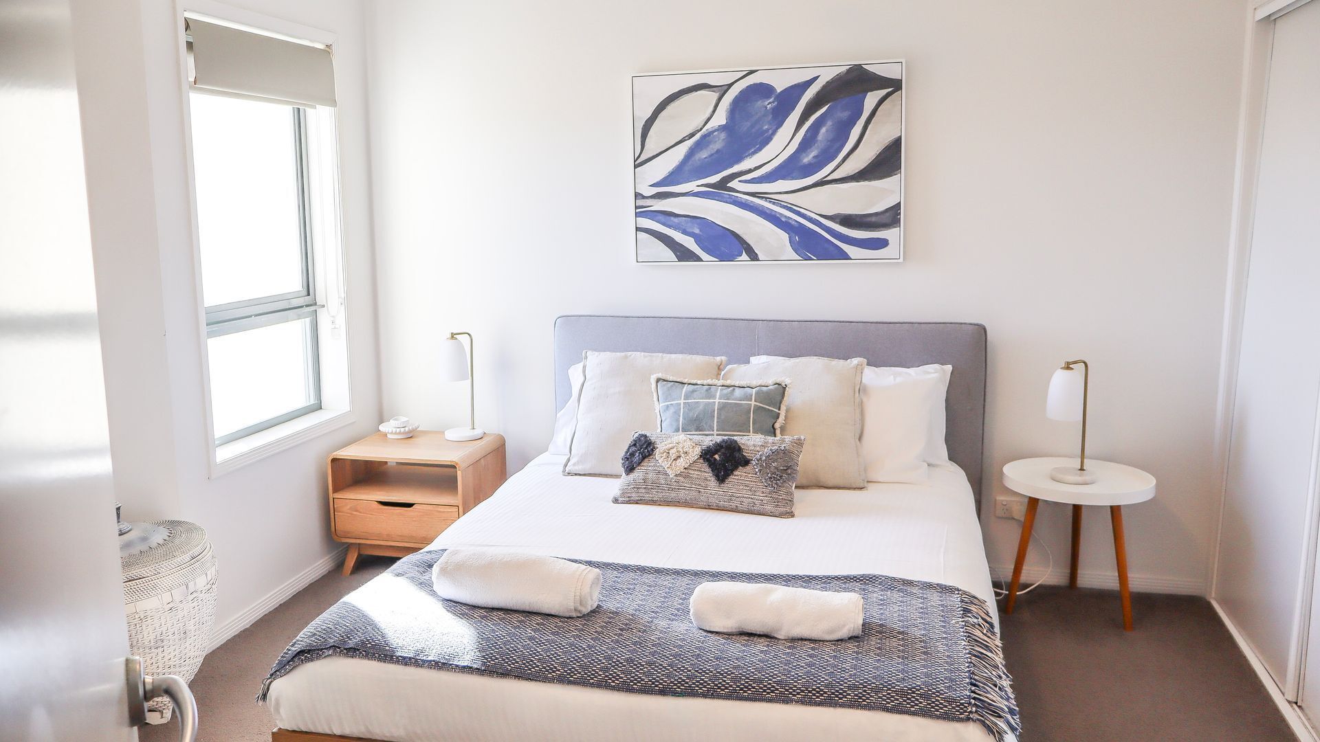 A modern bedroom with a bed, bedside tables, a window, and a wall art piece.
