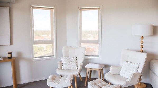 A room with two white armchairs, a small wooden table, and a lamp.